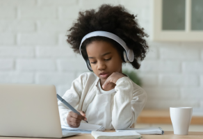 Girl with headphones works on Chromebook at kitchen table